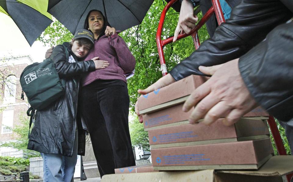 Emily Titon, a short white person, hugging Cheryl McCollins, a tall Black woman, in the rain, while unloading boxes with printed signatures on a petition to ban the shocks.